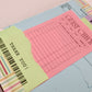 A close-up of a colorful stationery set featuring a light pink guest check pad, a light green thank you note with a barcode, and other matching receipt and ticket sheets.